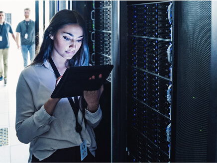 Woman standing in front of servers, viewing information on a tablet